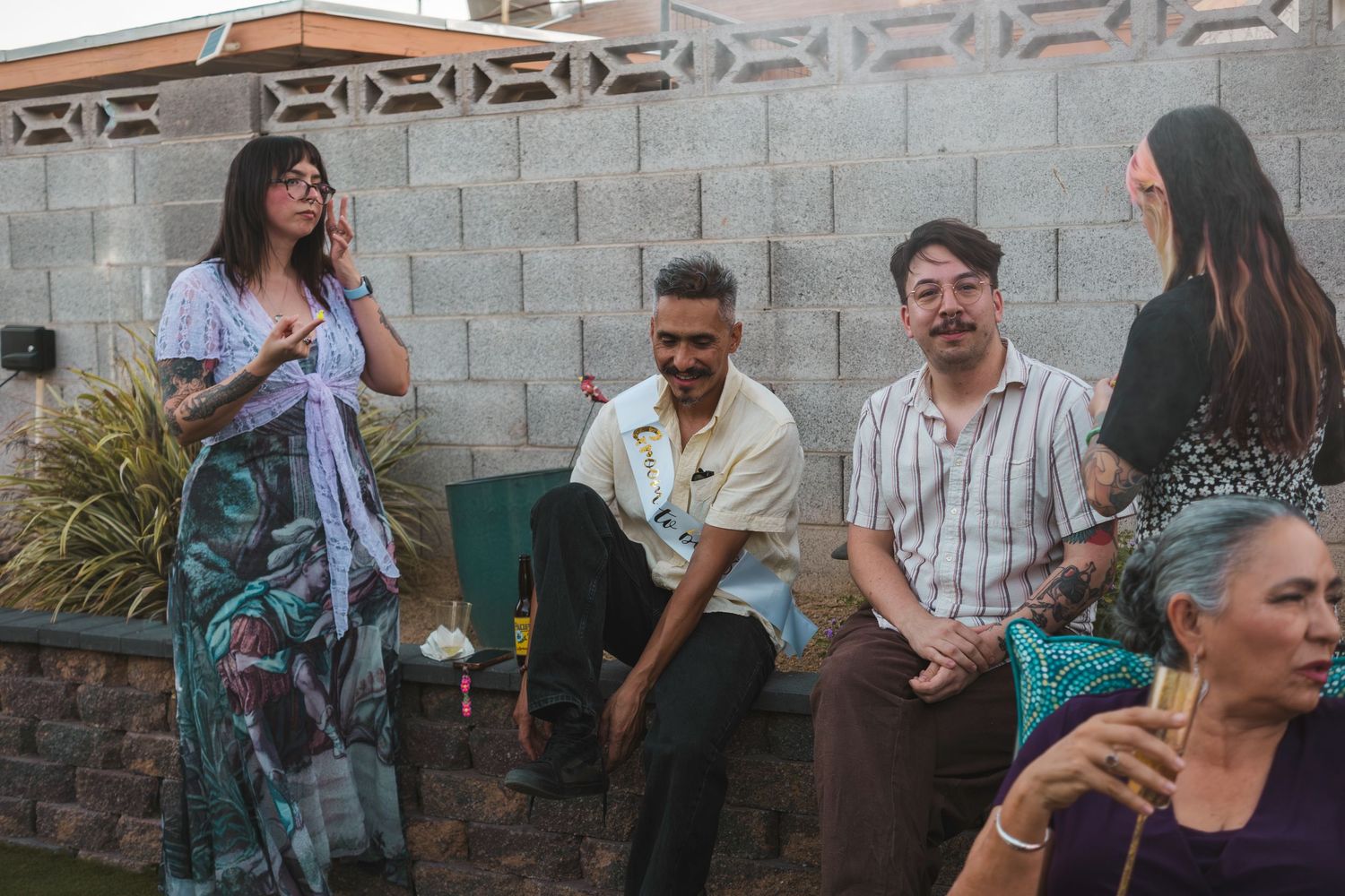 Group of friends socializing outdoors at a casual backyard gathering near a concrete block wall.