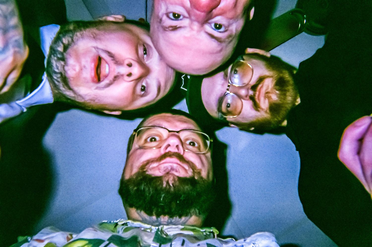 Four friends huddle together in a circle, looking down at the camera with playful expressions in a fun group photo.