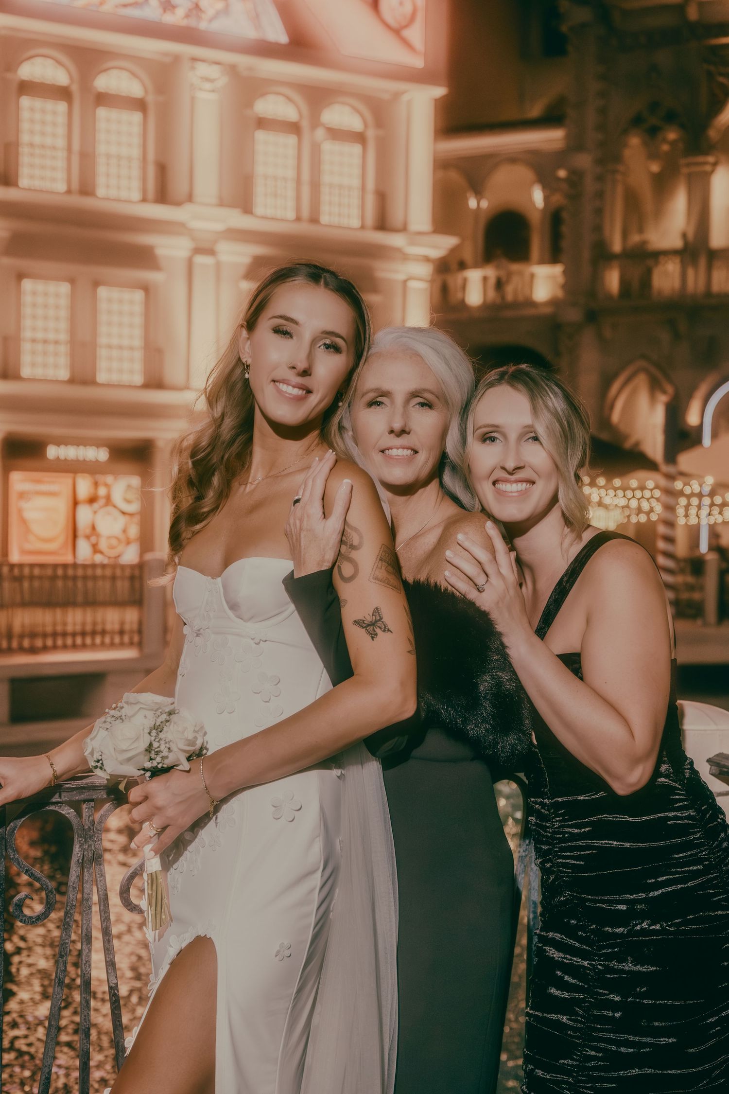 Bride in white gown smiles with two women in black dresses at elegant Las Vegas casino wedding venue.