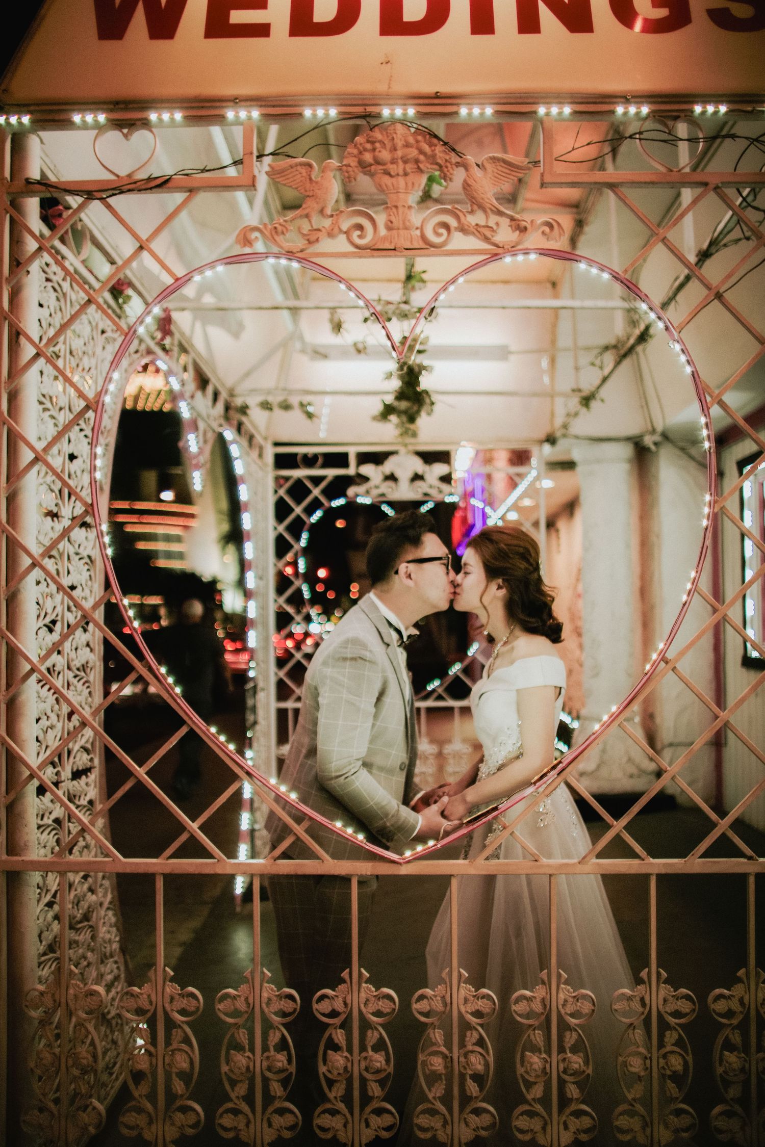 Couple kissing inside a glowing heart-shaped frame at a Las Vegas wedding chapel at night.