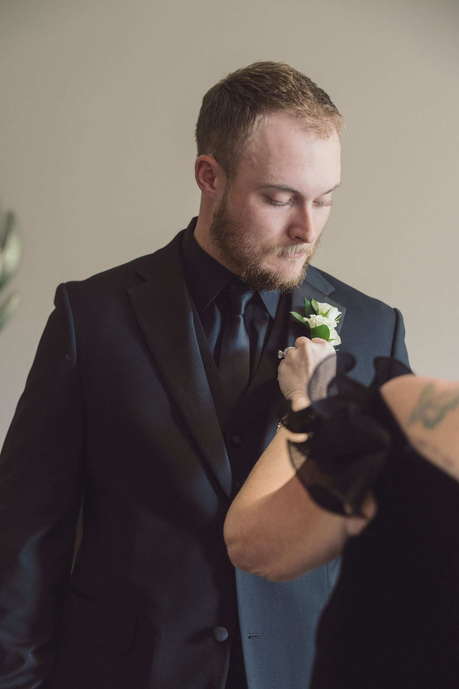 Groom in black suit having white floral boutonniere pinned to lapel.