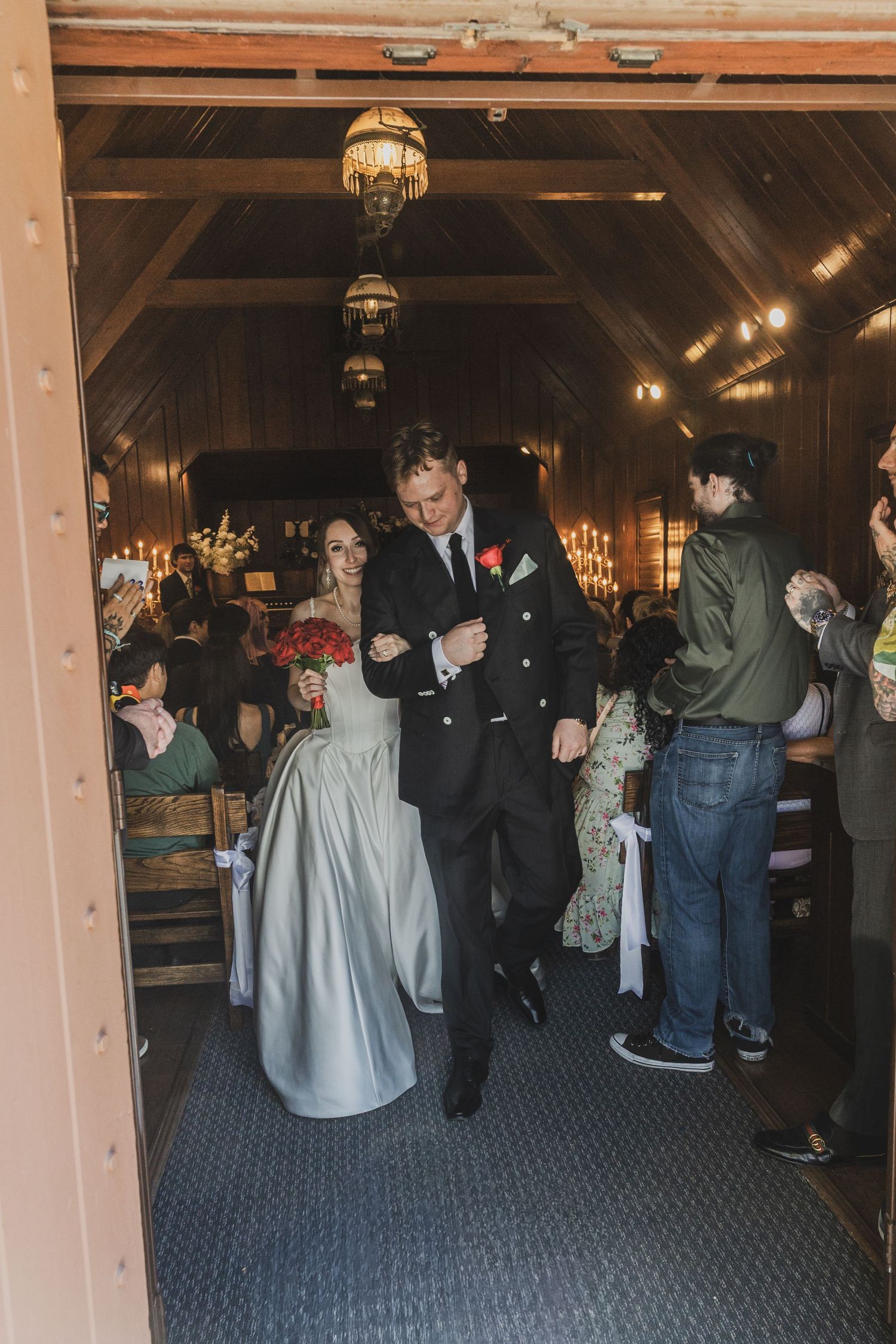 Bride and groom walk down the aisle in a rustic barn wedding venue, guests seated on wooden pews.