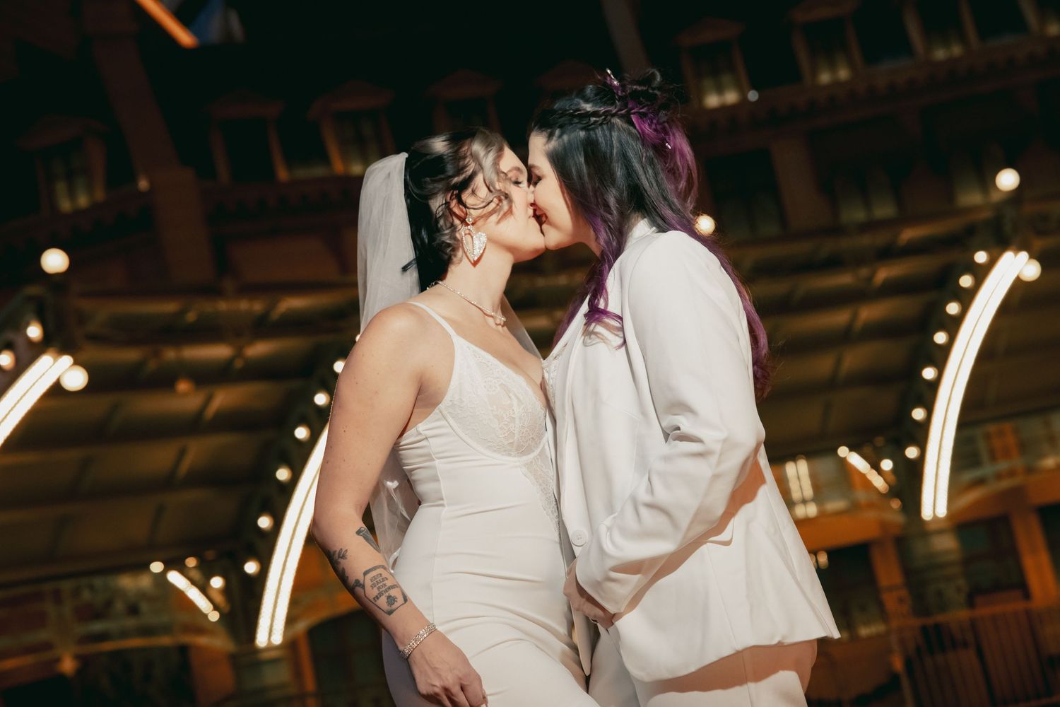 Two brides share a passionate kiss under warm lights at a Las Vegas wedding venue.