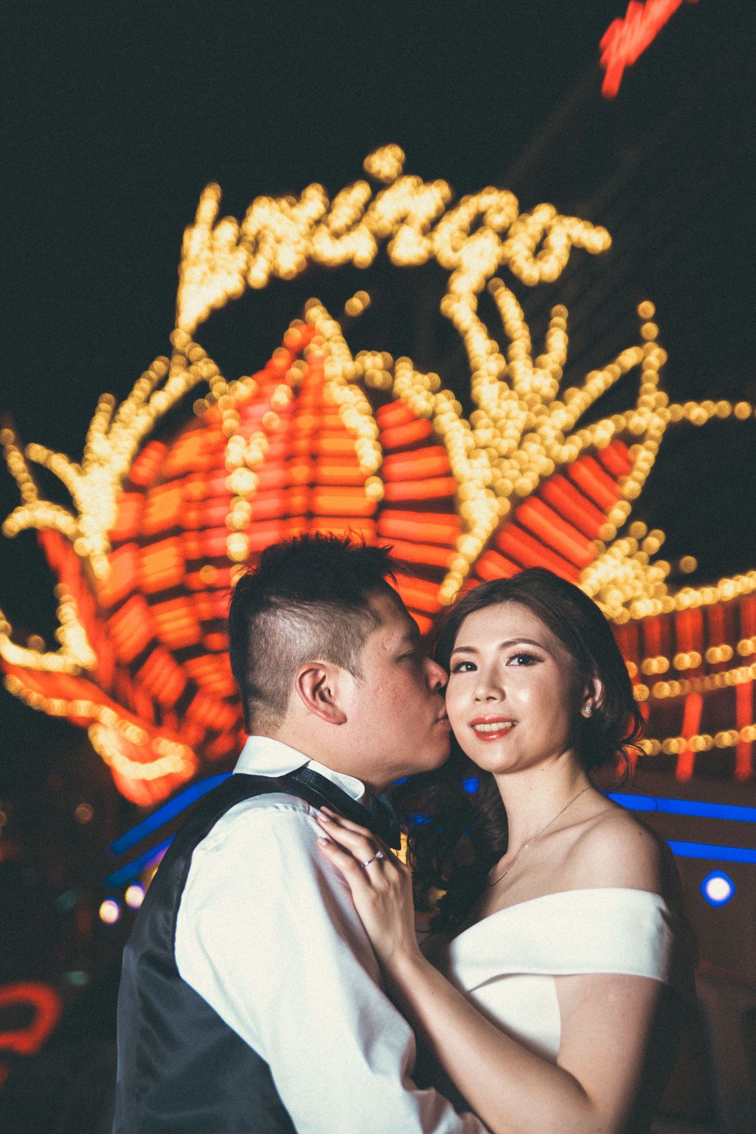 Bride and groom sharing romantic kiss in front of illuminated Flamingo casino sign at night in Las Vegas.
