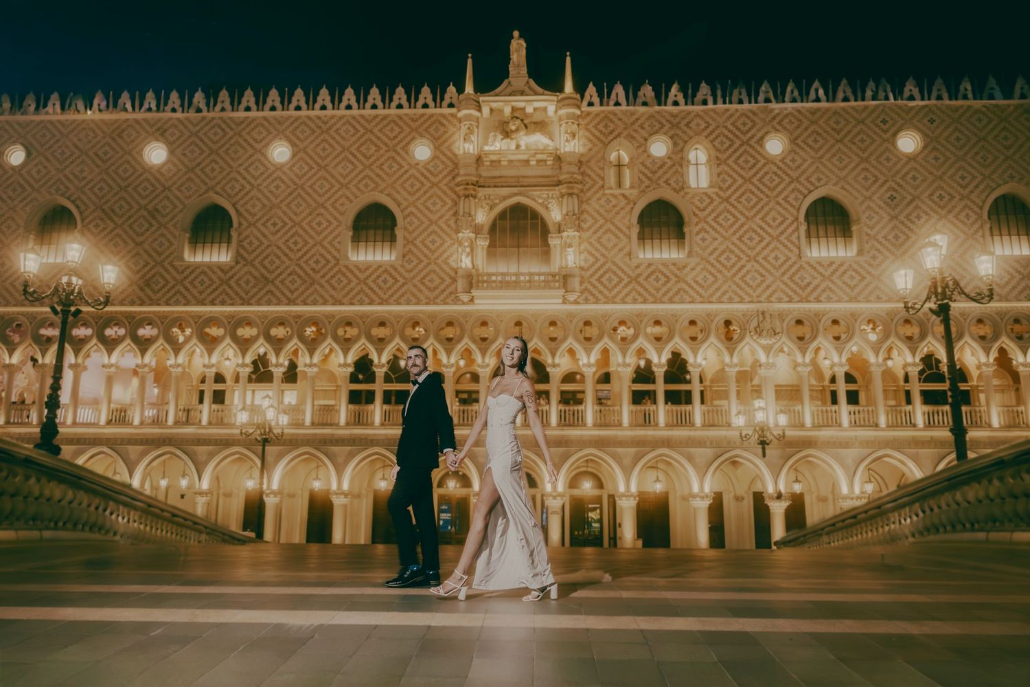 Bride and groom posing before the stunning lit facade of The Venetian Las Vegas at night.