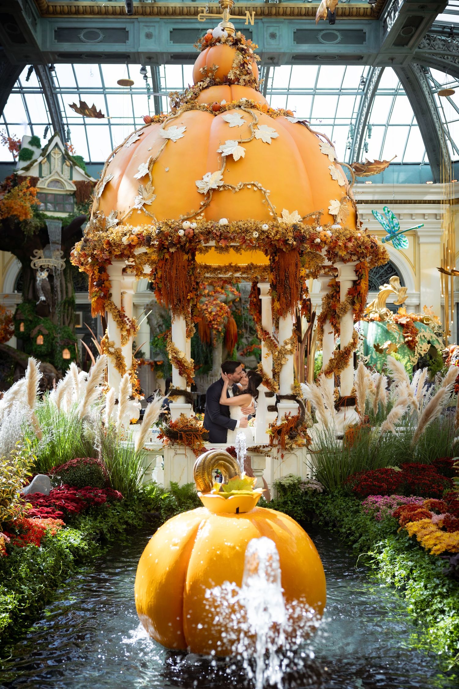 Couple kisses inside an elaborate pumpkin-themed gazebo with fountain at Bellagio conservatory.