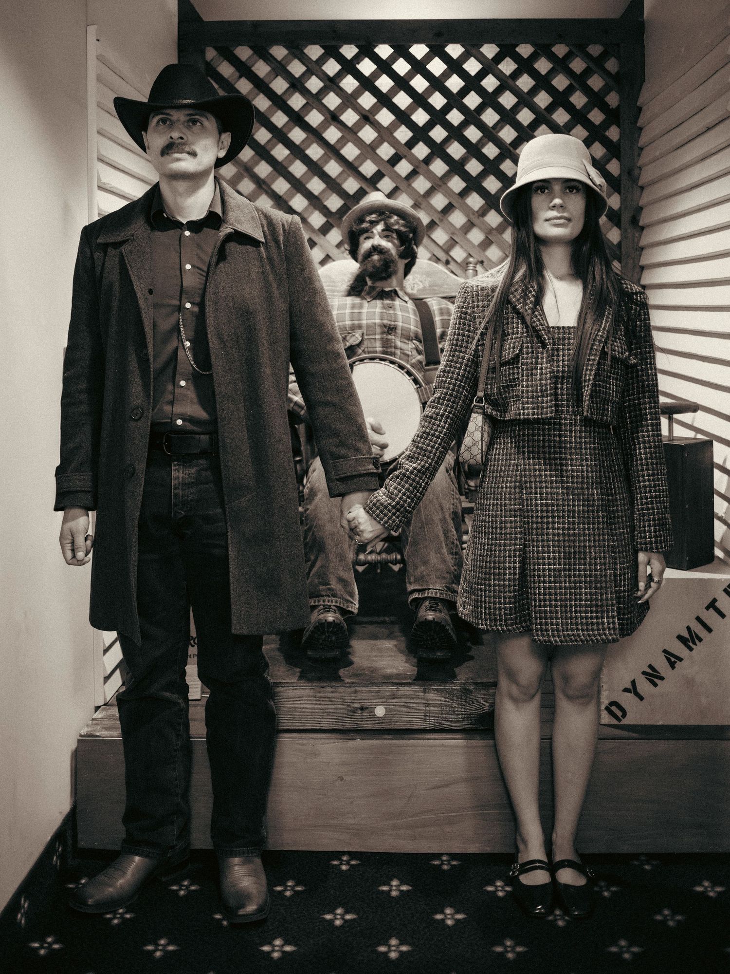 Vintage sepia photo of a couple in retro western attire holding hands with a dog posed between them.
