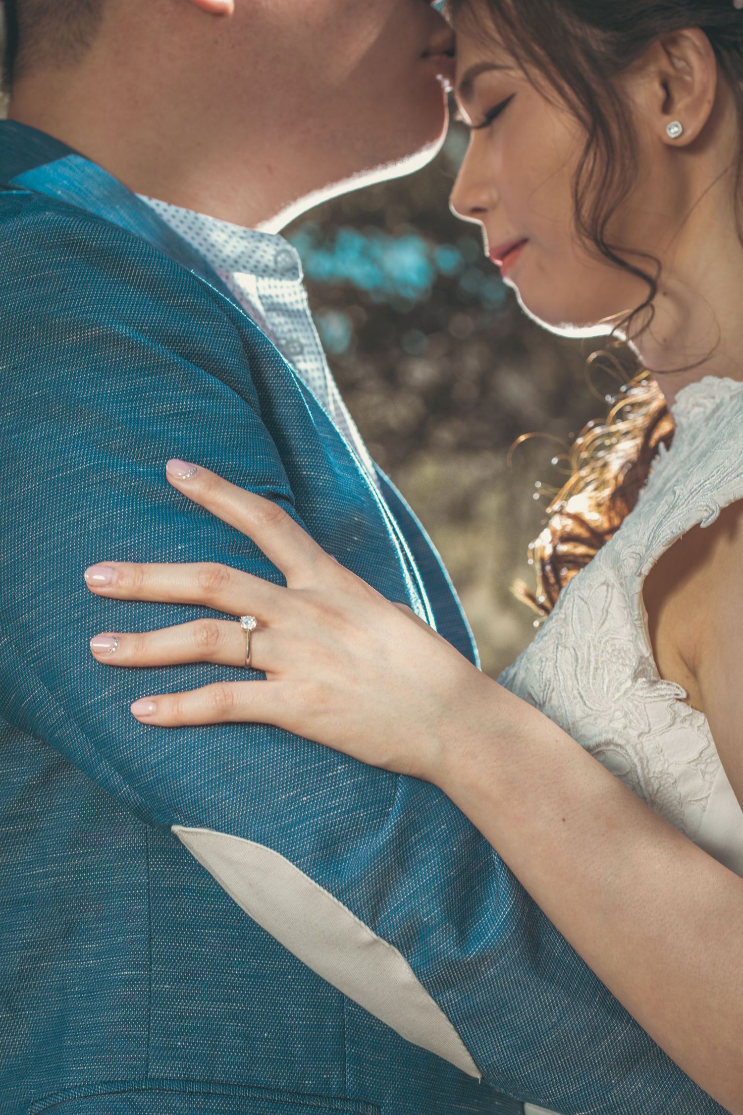 Bride and groom sharing an intimate moment, her hand resting on his blue suit, diamond engagement ring visible.