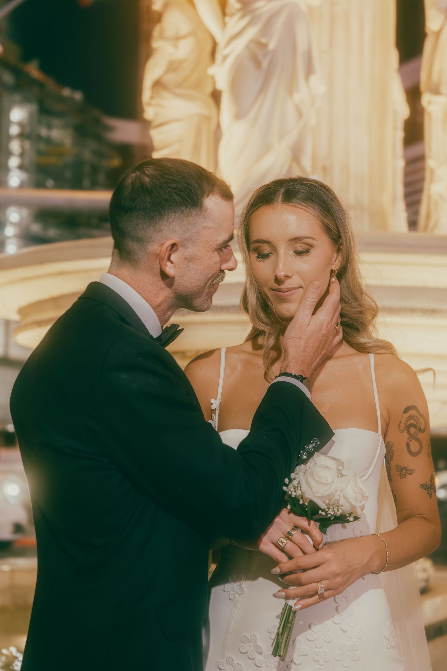 Groom tenderly holds bride's face while she closes her eyes, holding white rose bouquet at Las Vegas wedding.