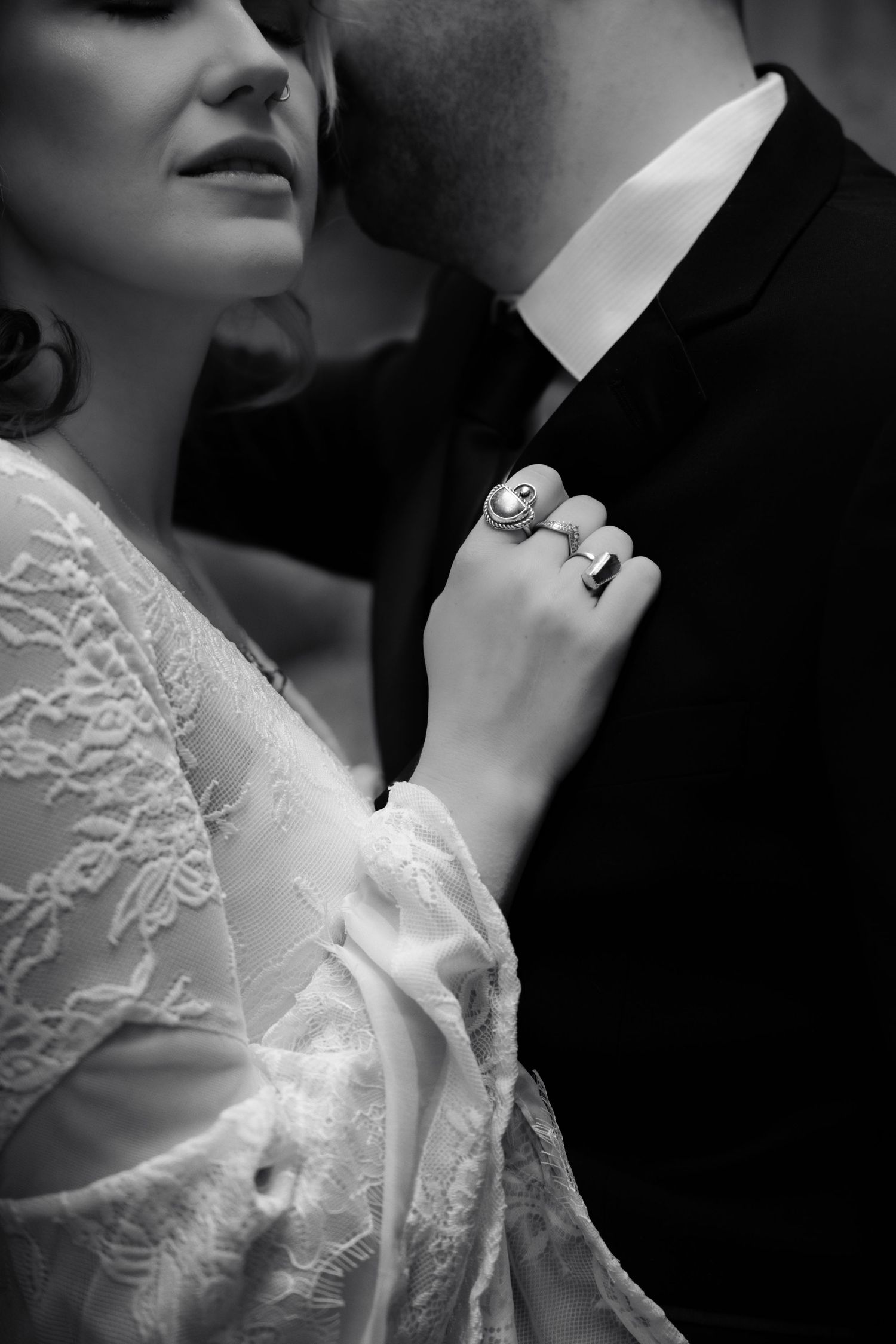 Black and white close-up of bride with statement rings holding grooms tuxedo lapel tenderly.