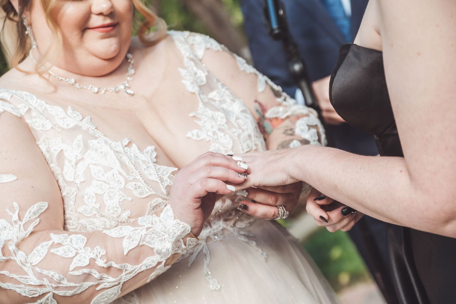 Bride in lace wedding gown receiving ring during outdoor wedding ceremony.