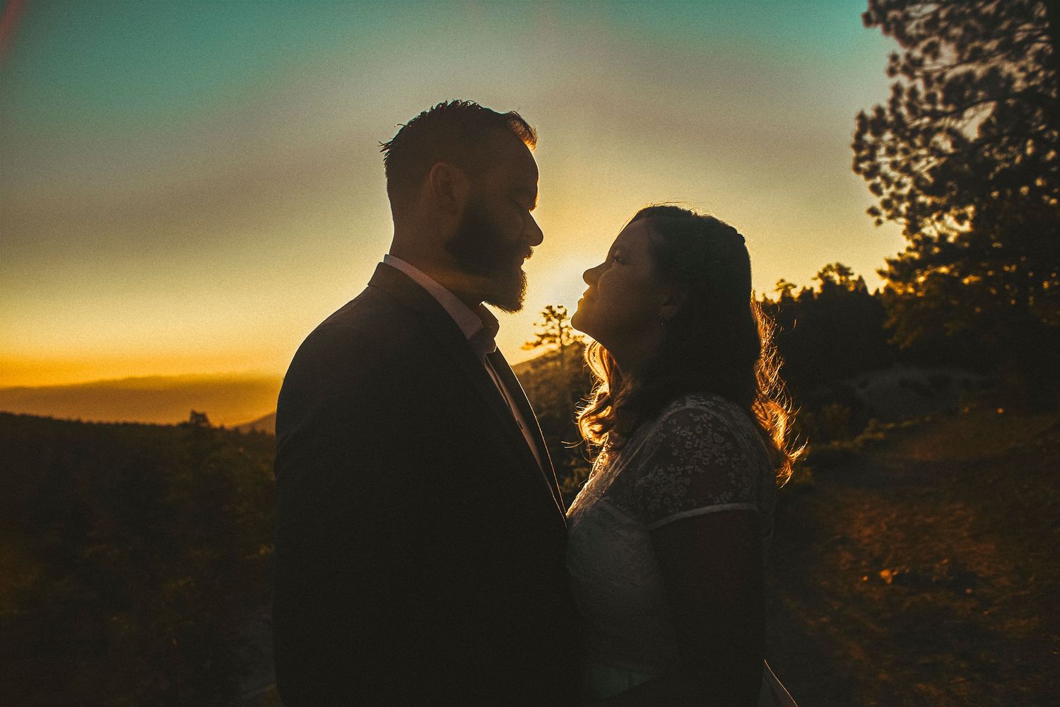 Romantic couple silhouetted against a golden sunset sky, sharing an intimate moment outdoors at dusk.