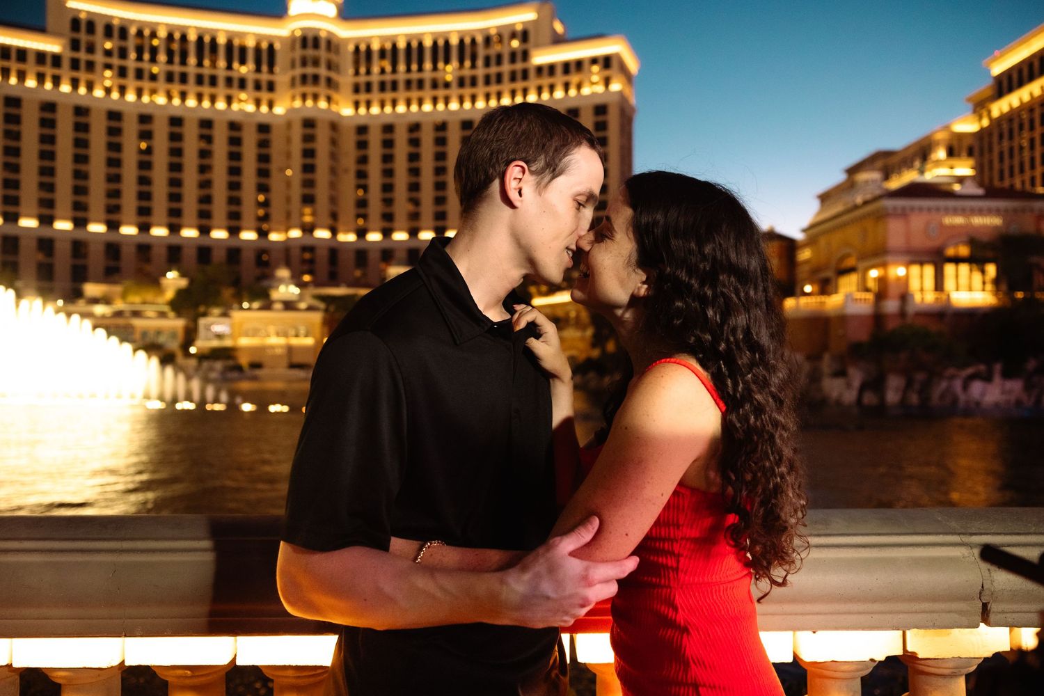 Romantic couple nearly kissing in front of illuminated Bellagio hotel fountains at night in Las Vegas.