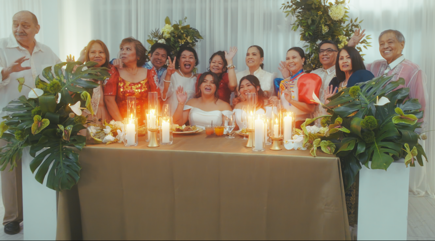 Large family group photo at a wedding reception table with candles and tropical floral arrangements.