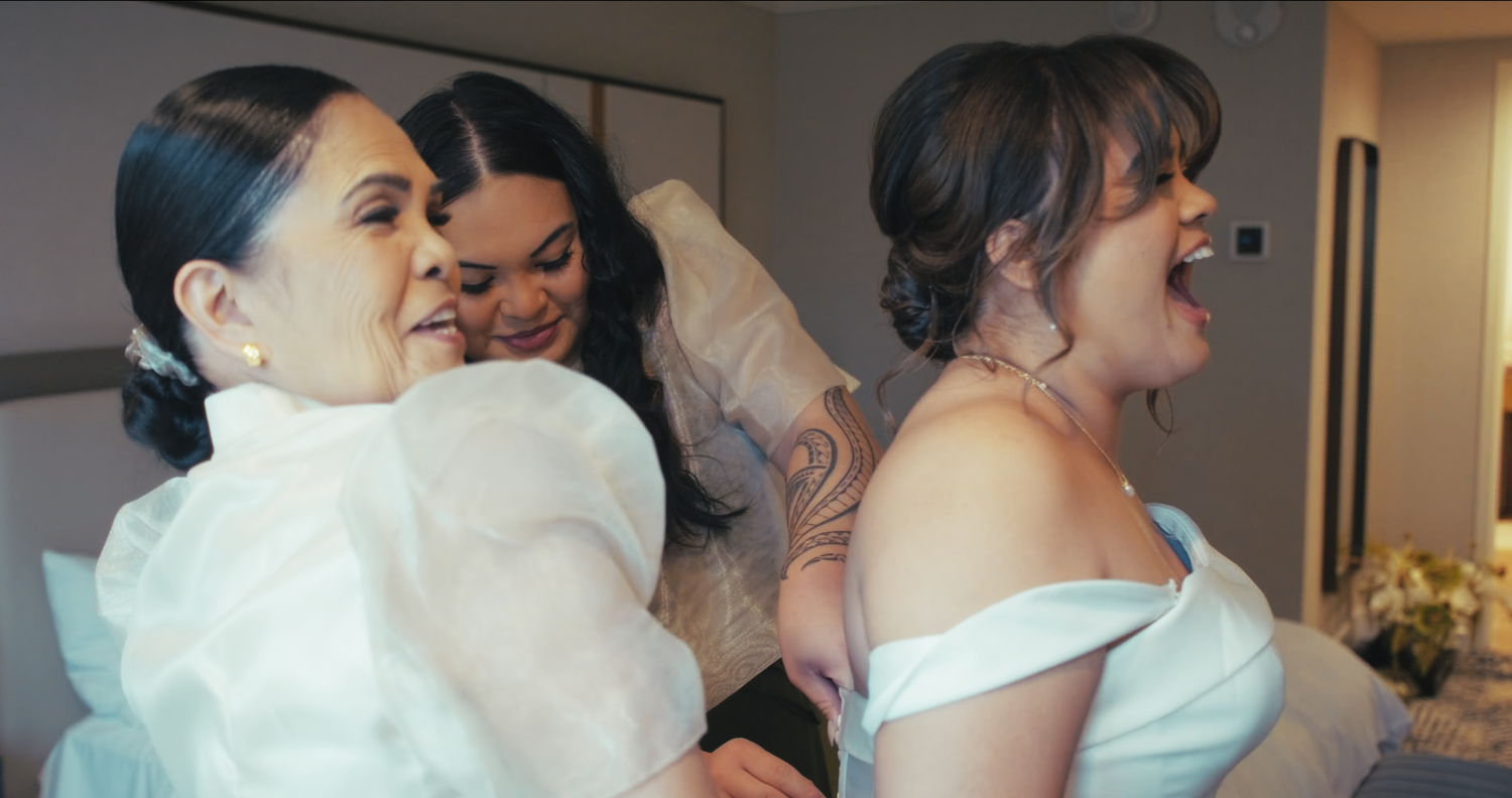 Three women in wedding attire laugh and embrace joyfully during bridal preparations.