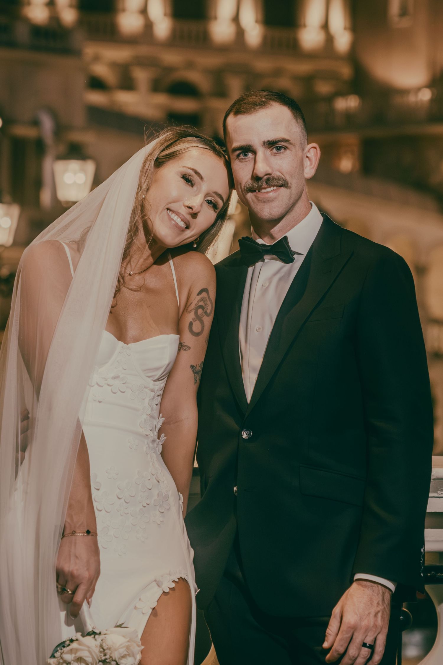 Tattooed bride in a white dress and groom with mustache pose together smiling inside a Las Vegas venue.