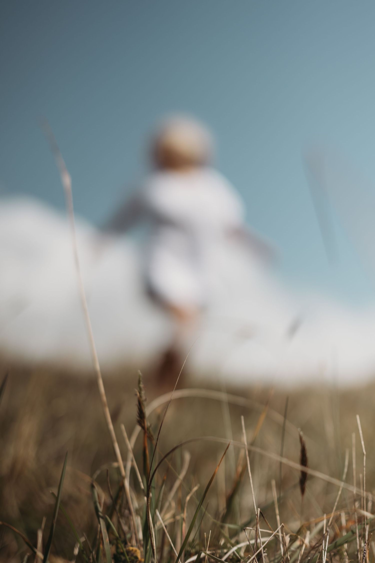 Blurred figure in white dress running through a golden grass field under a blue sky.
