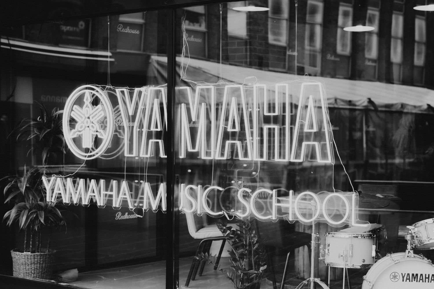 Black and white storefront photo of a Yamaha Music School with neon signage visible through the window.