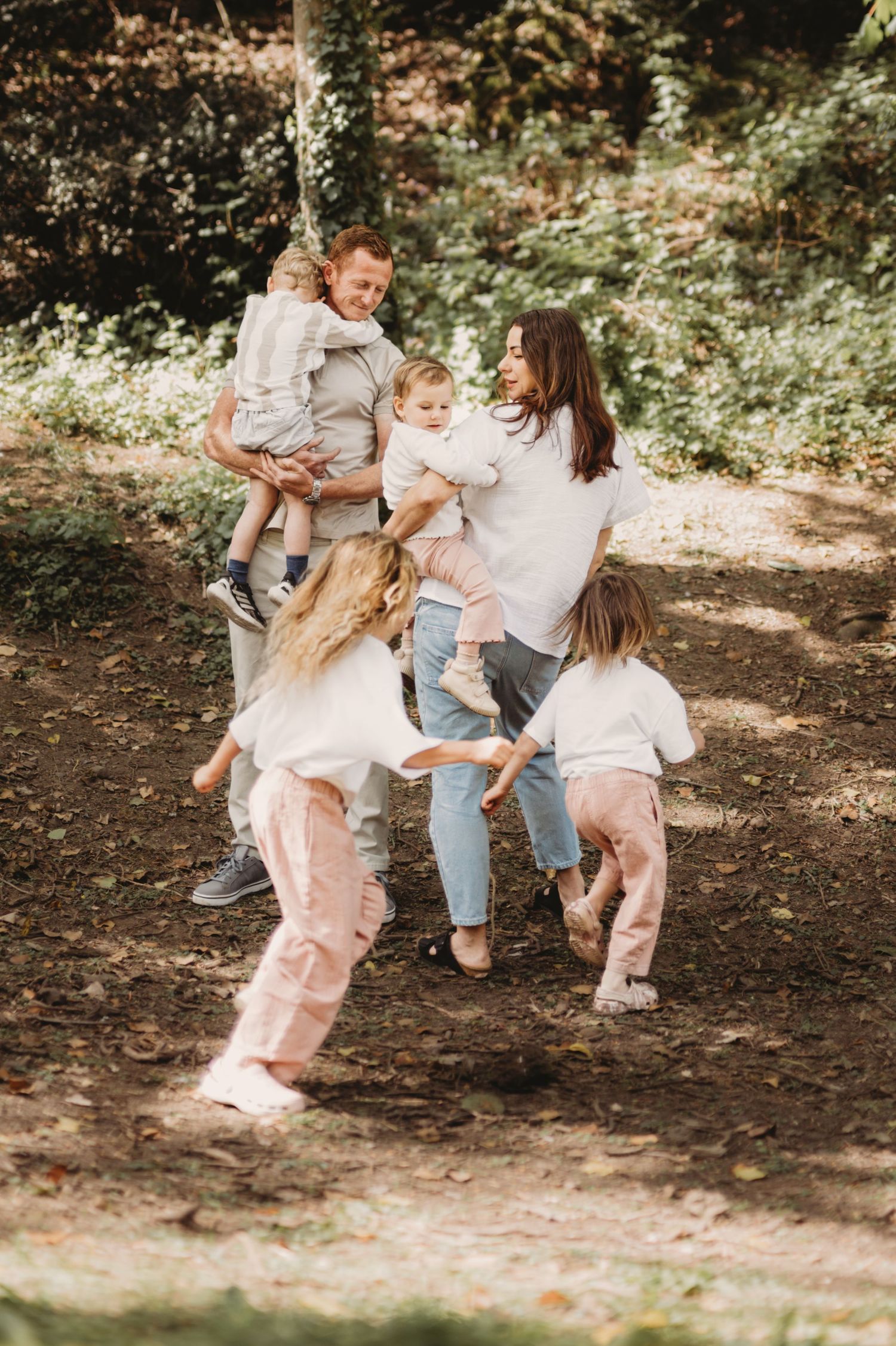 Happy family with children playing together on forest woodland path.
