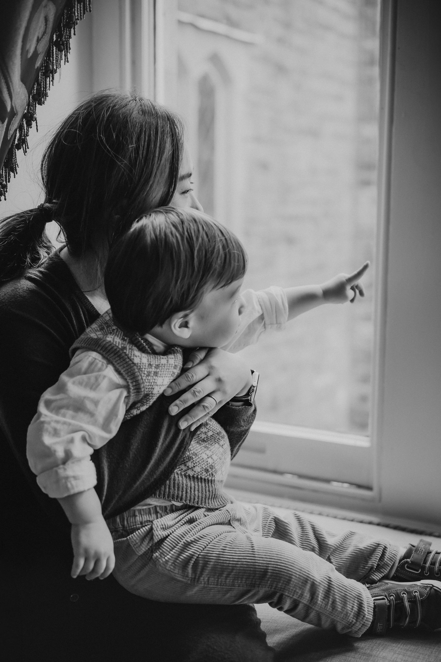Black and white photo of a mother and toddler sitting by a window as the child points outside.