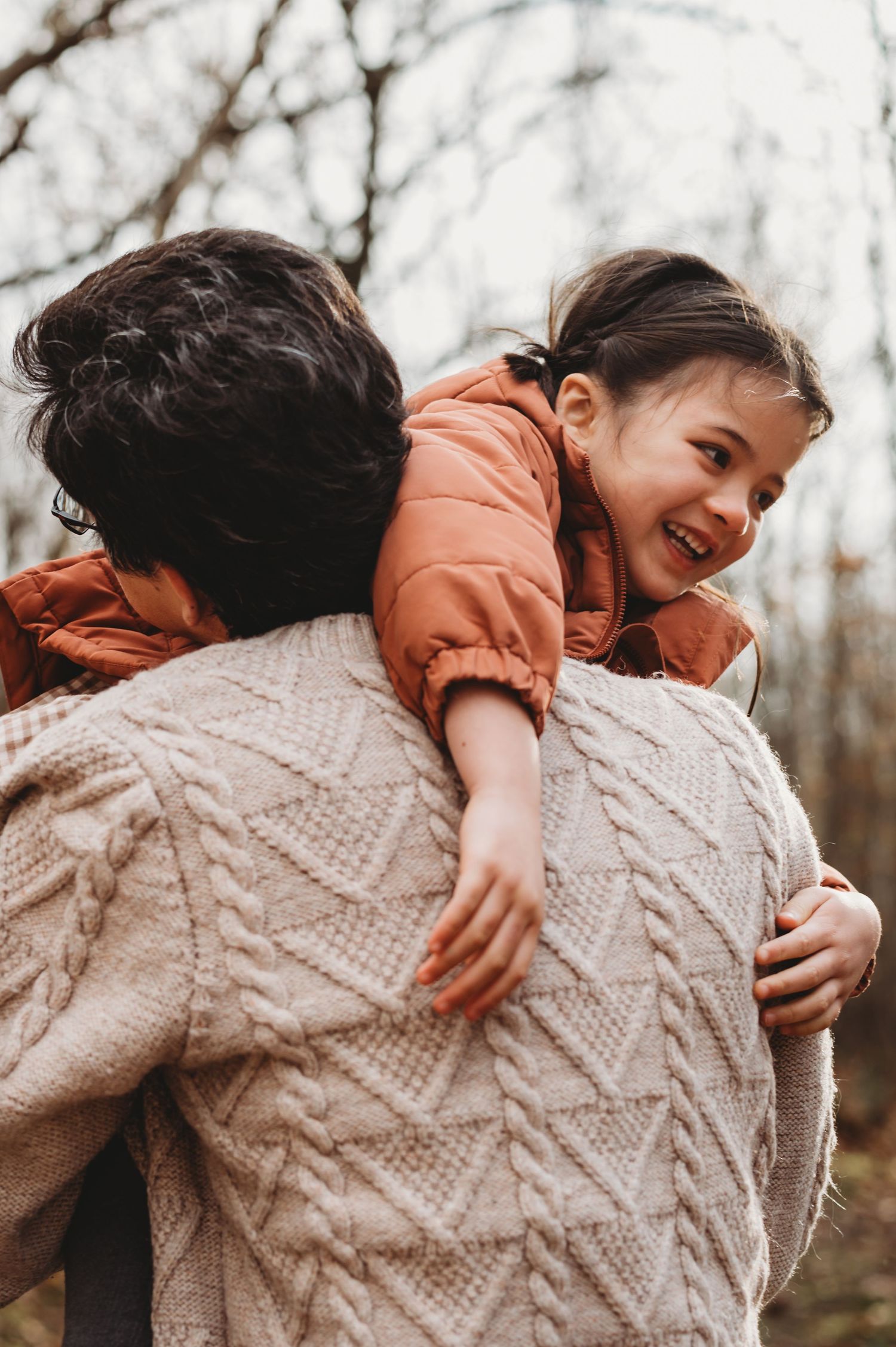 Happy young girl laughing while being carried on an adult's back in an autumn forest.