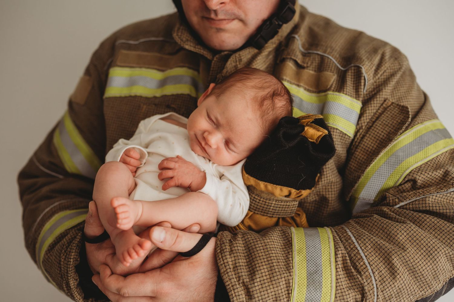 Sleeping newborn baby resting peacefully in the arms of a parent wearing a firefighter uniform.