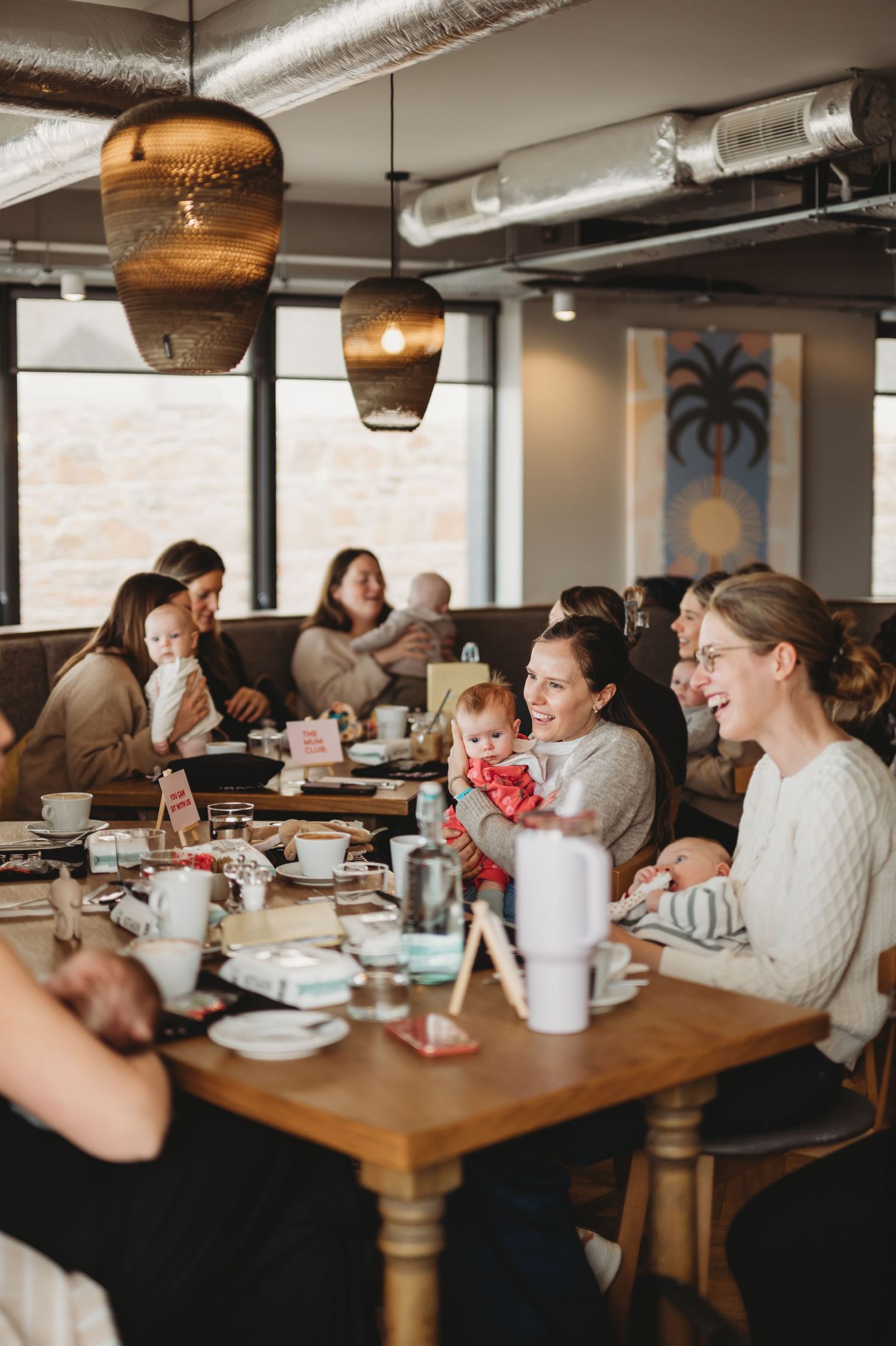 Happy mothers with infants sharing smiles at a casual restaurant meetup event.