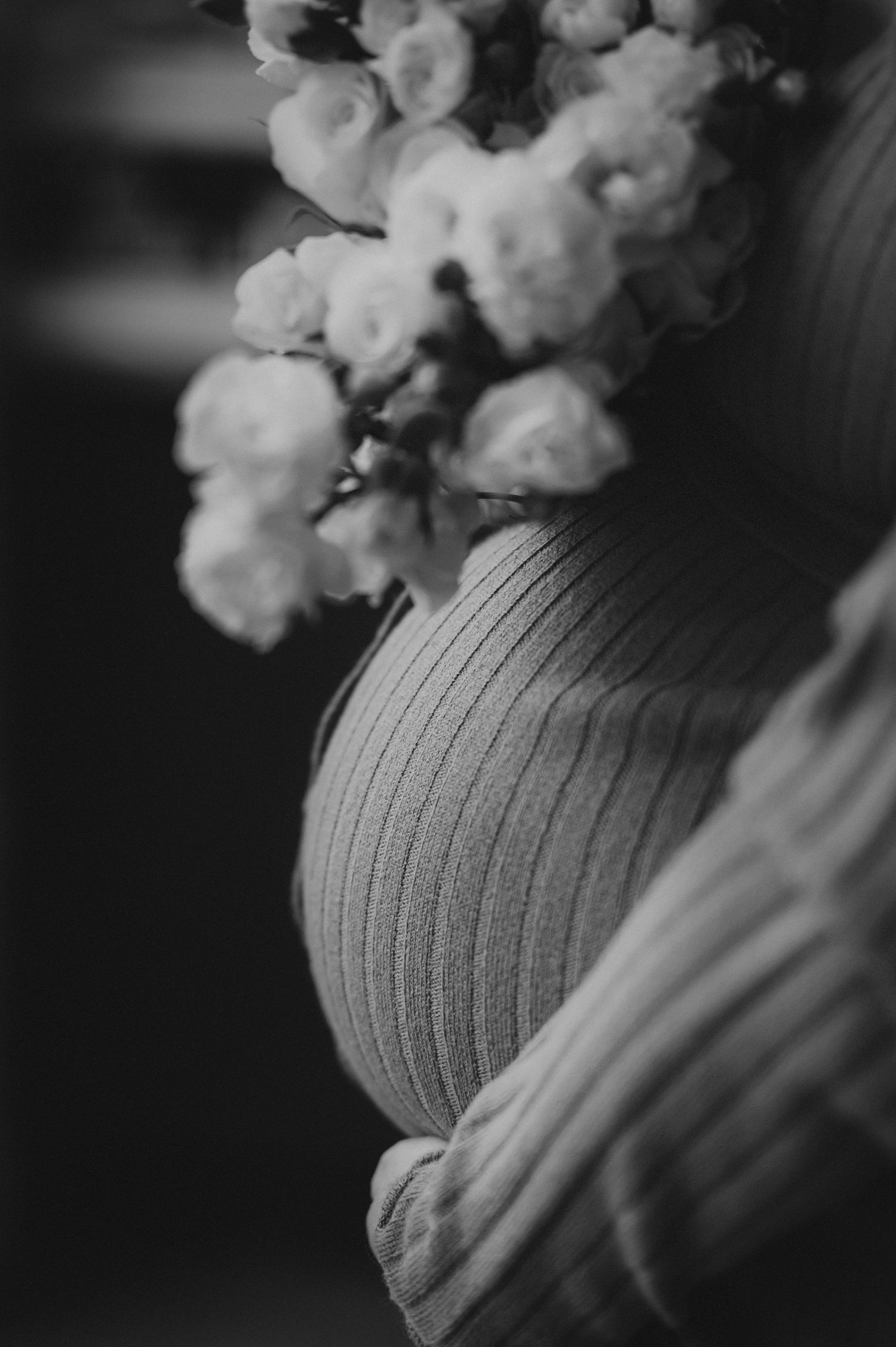 Black and white close-up of a pregnant belly in a ribbed sweater adorned with white flowers.