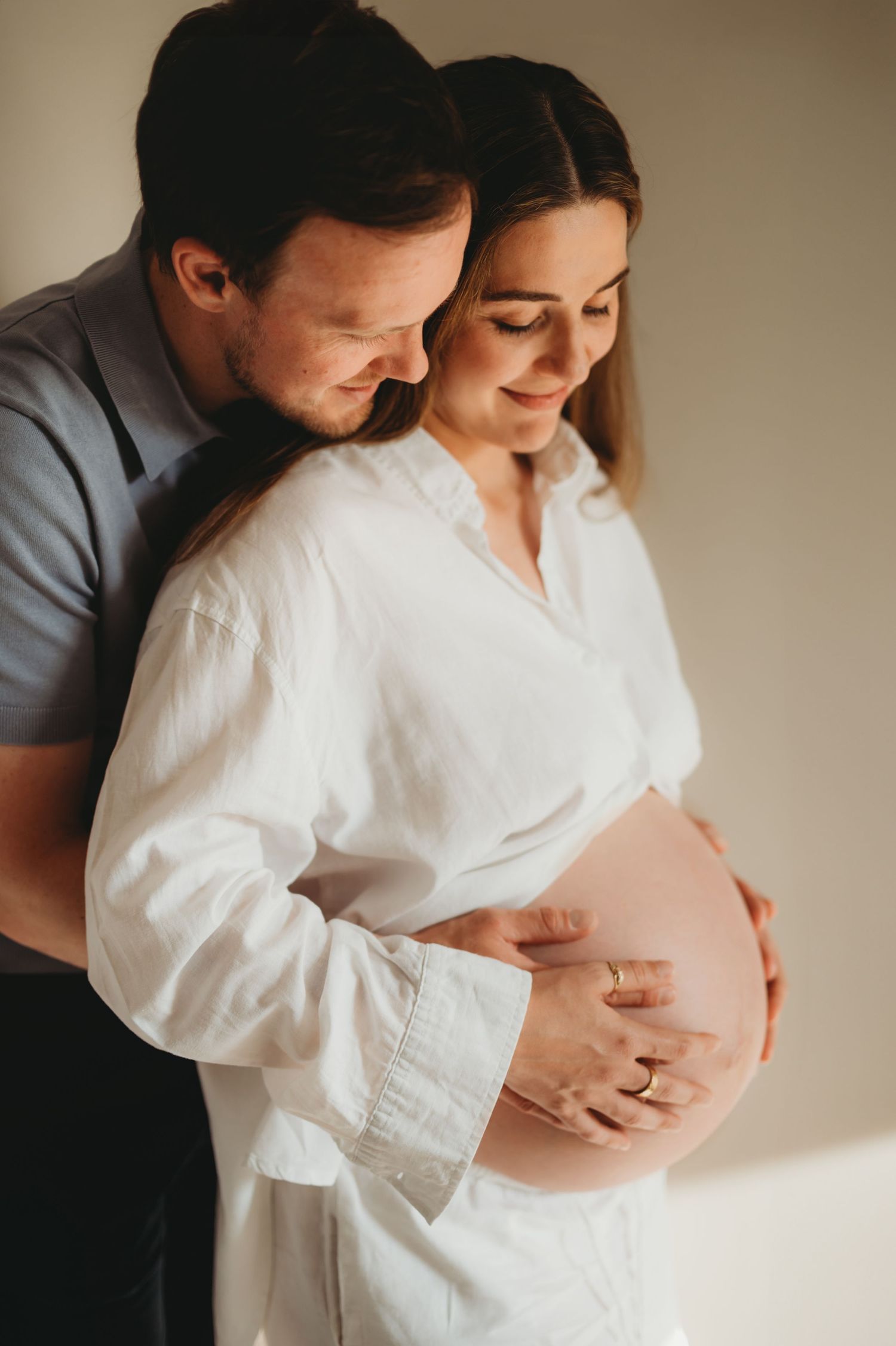 Couple tenderly cradling pregnant belly together indoors.