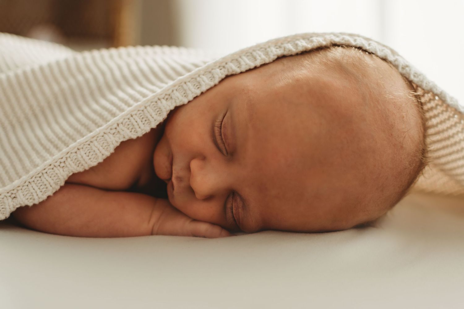 Peaceful newborn baby sleeping on white surface covered with a soft striped blanket.