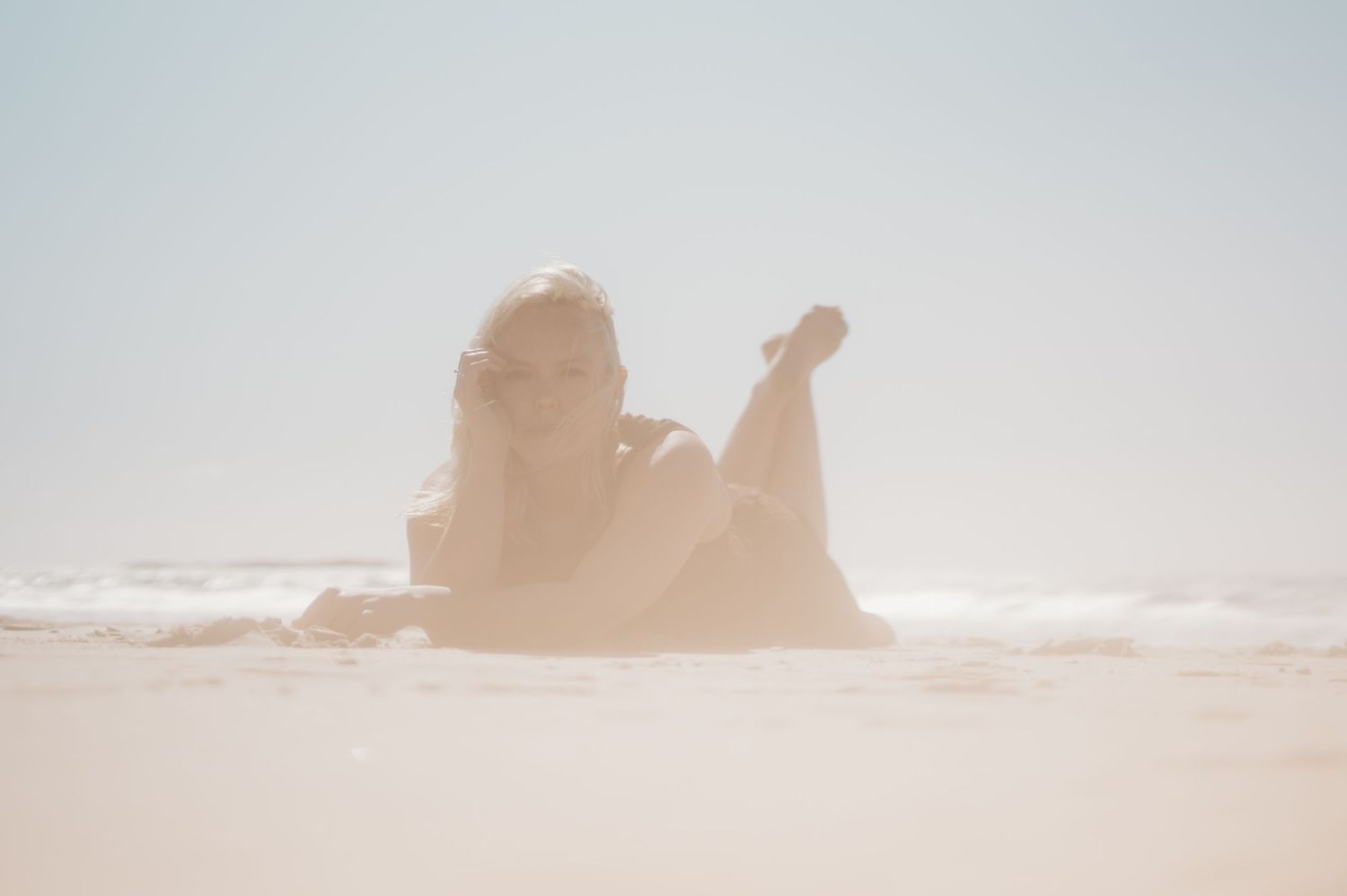 Overexposed dreamy photo of woman relaxing on bright sandy beach by the ocean.