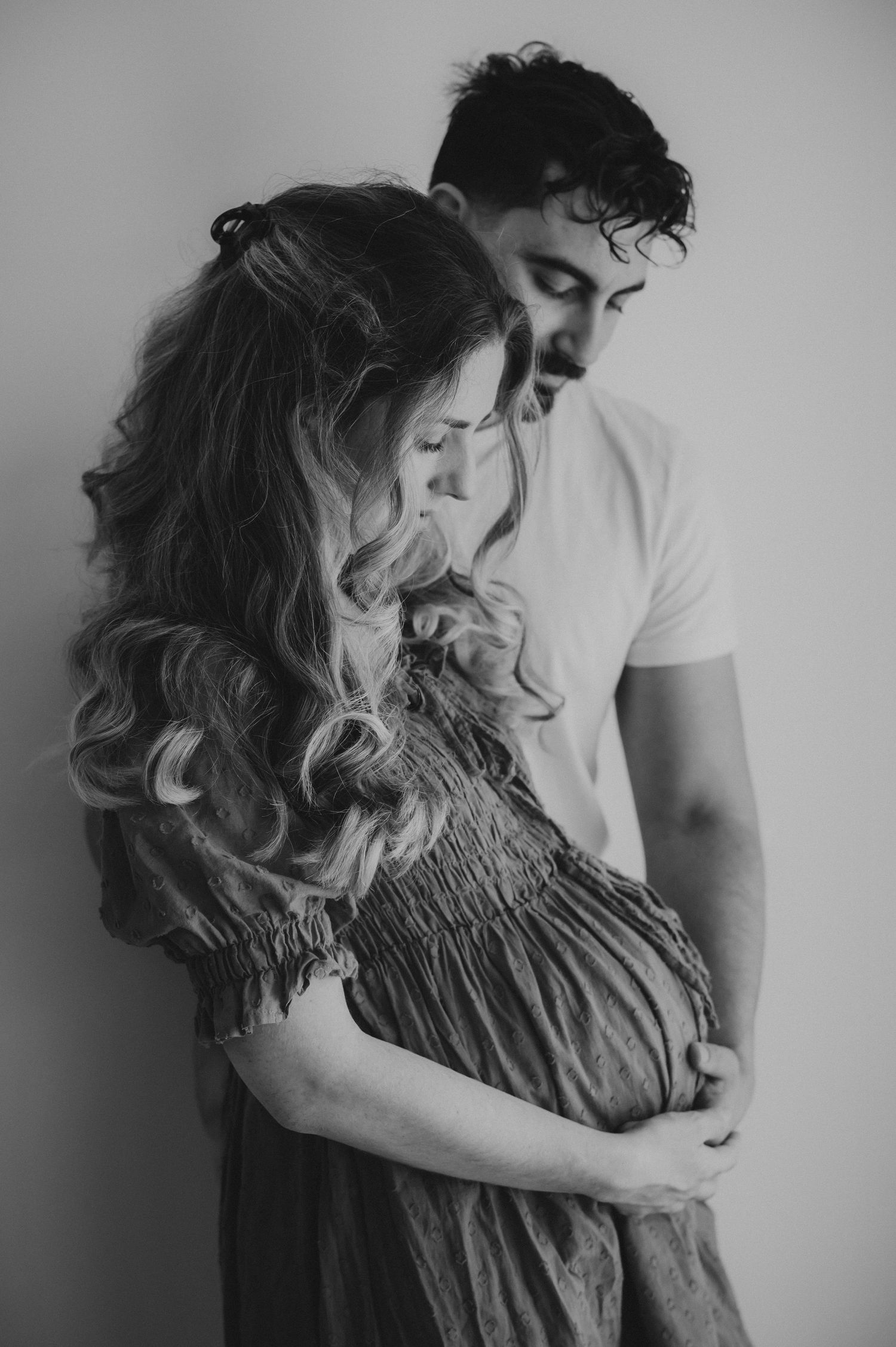 Black and white maternity photo of a couple tenderly embracing while cradling a pregnant belly.