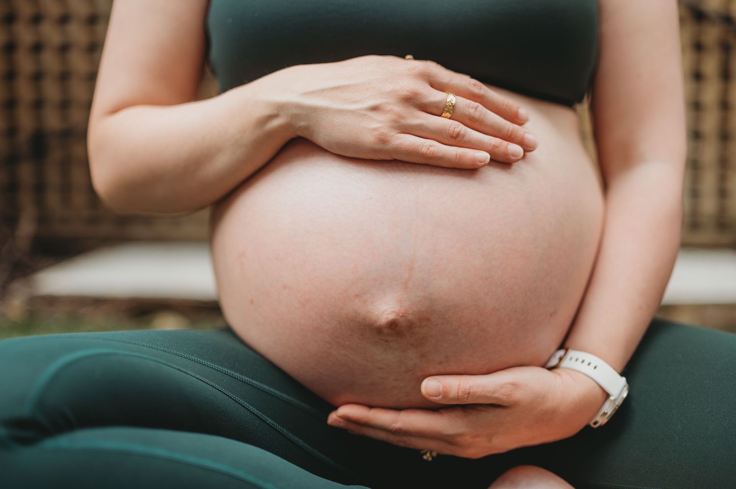 Close-up of pregnant woman in green outfit gently holding baby bump.