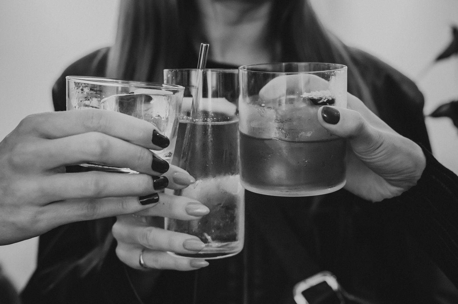 Woman with dark nail polish holding two ice-filled cocktail glasses in black and white photo.