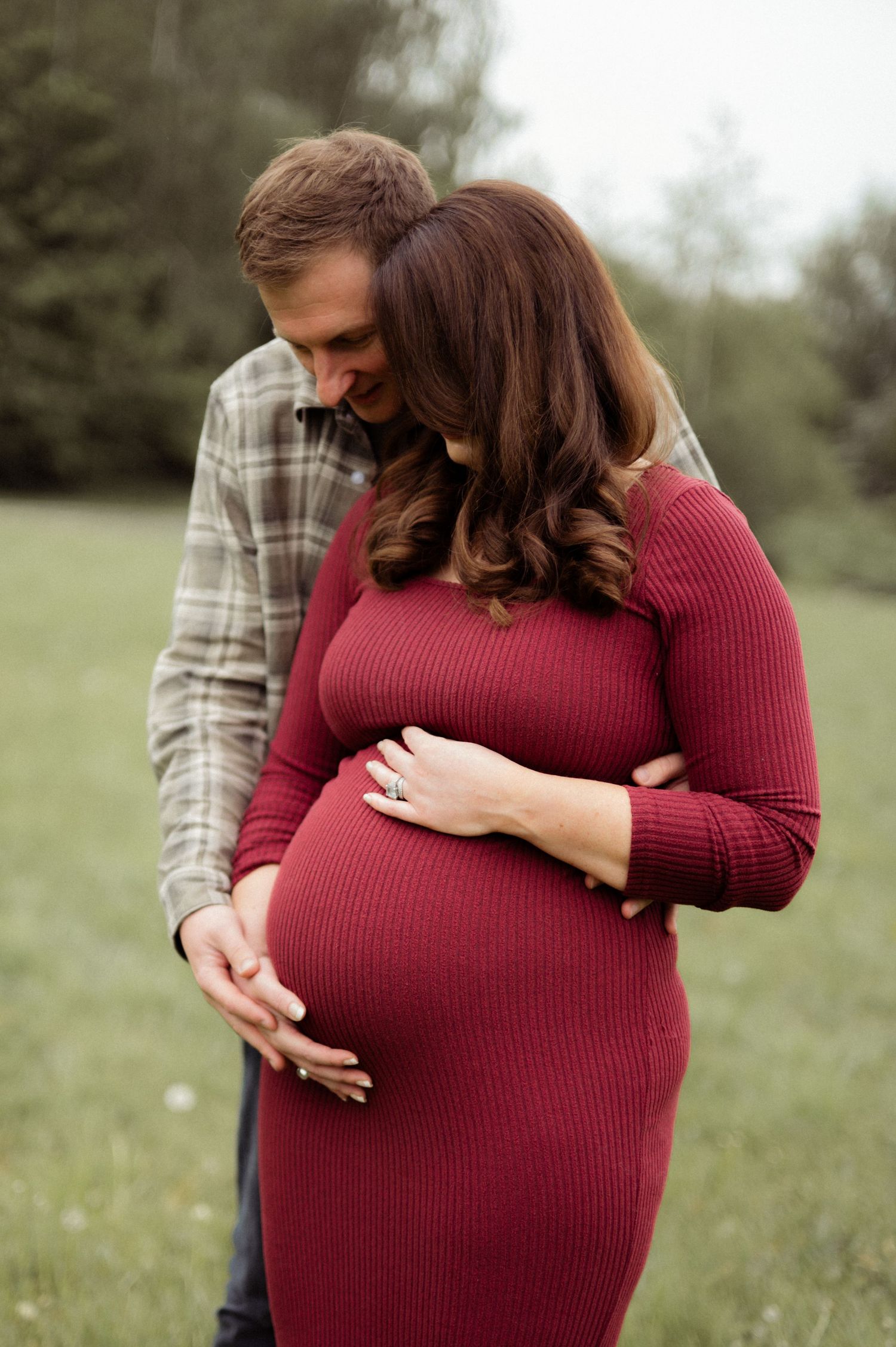 Couple embracing pregnant belly outdoors in green field maternity photo.