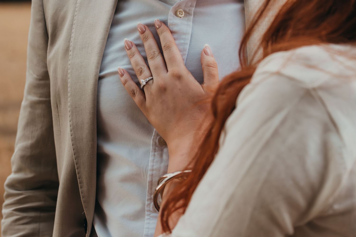 Close-up of a woman's hand with rings resting on a man's chest during a romantic moment.