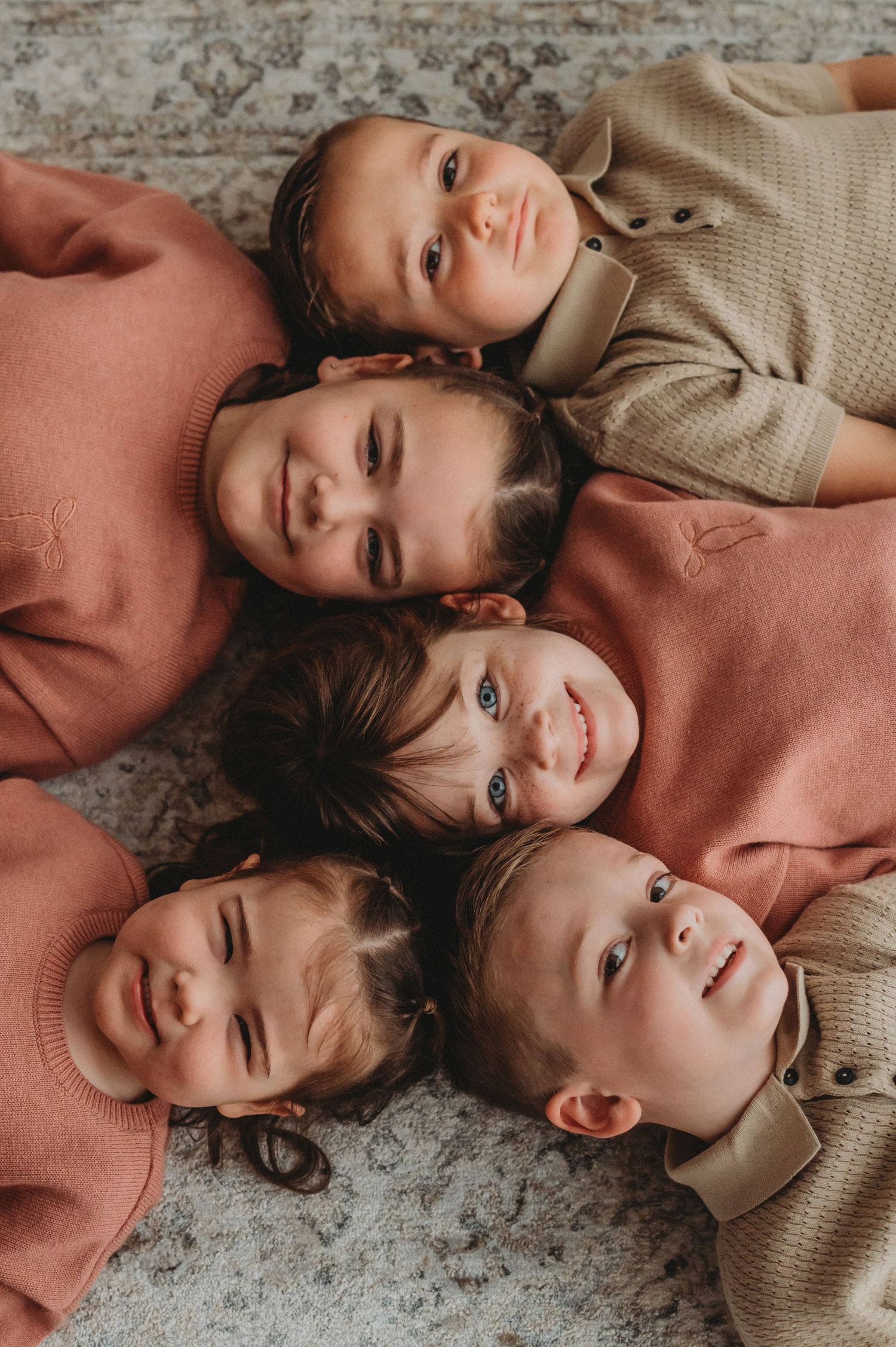 Five young children lying heads together on a carpet smiling upward.