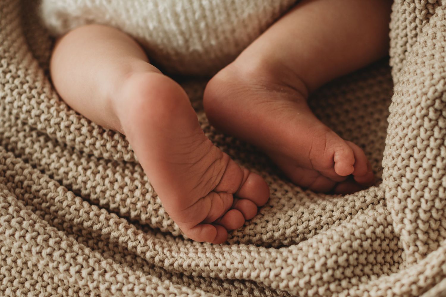 Close-up of adorable newborn baby feet resting on a textured cream knit blanket.