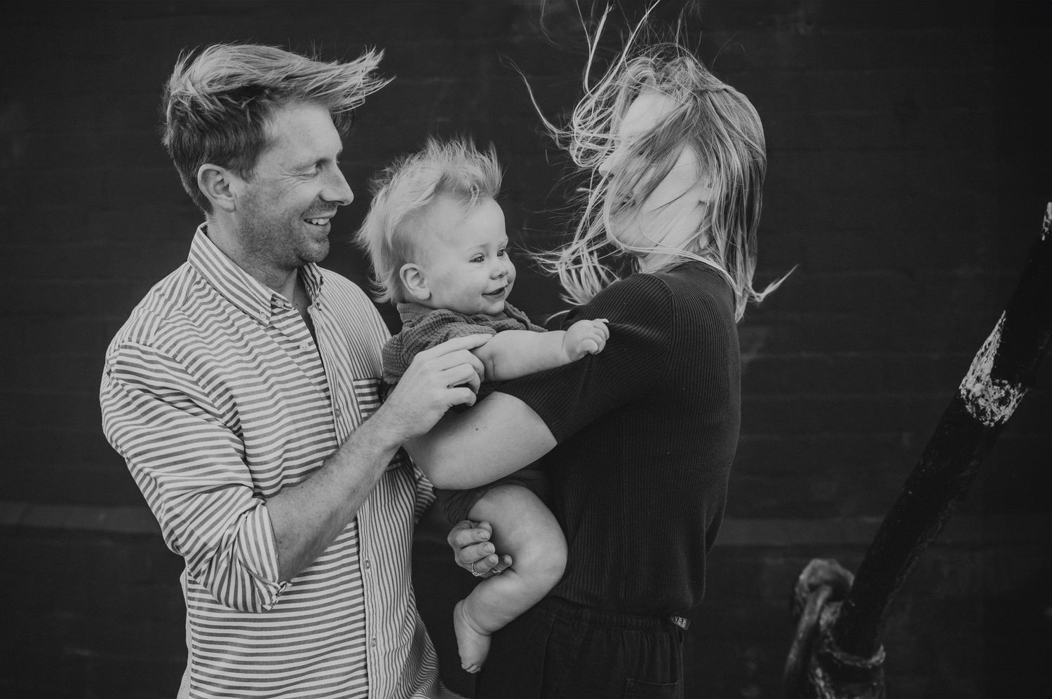 Black and white photo of happy parents with baby laughing together outdoors.