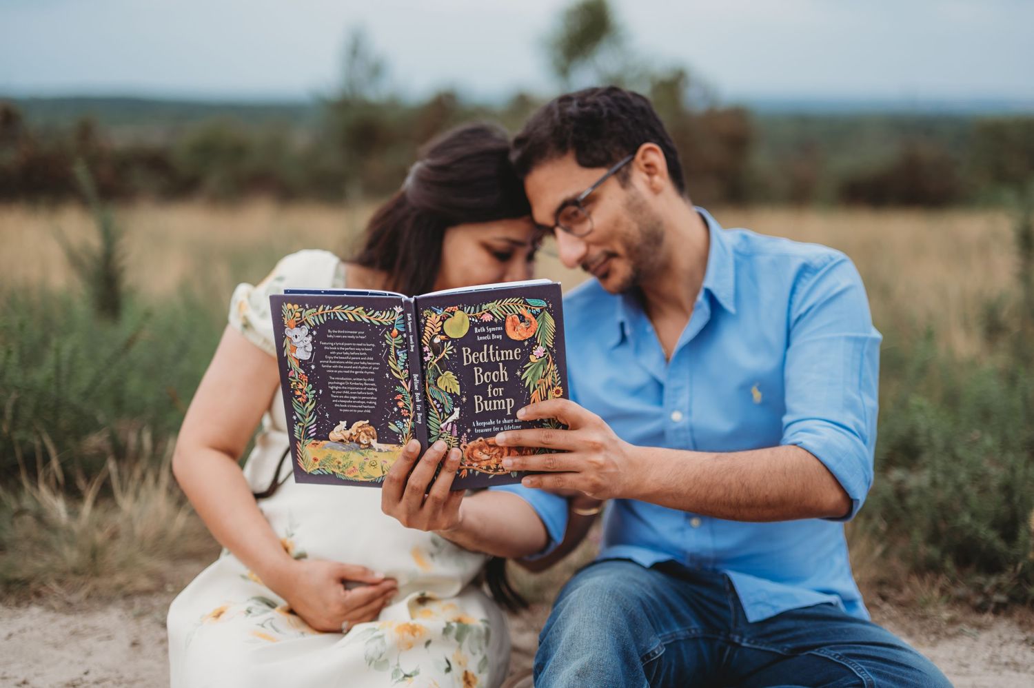 Expecting couple sitting outdoors reading bedtime stories book together.