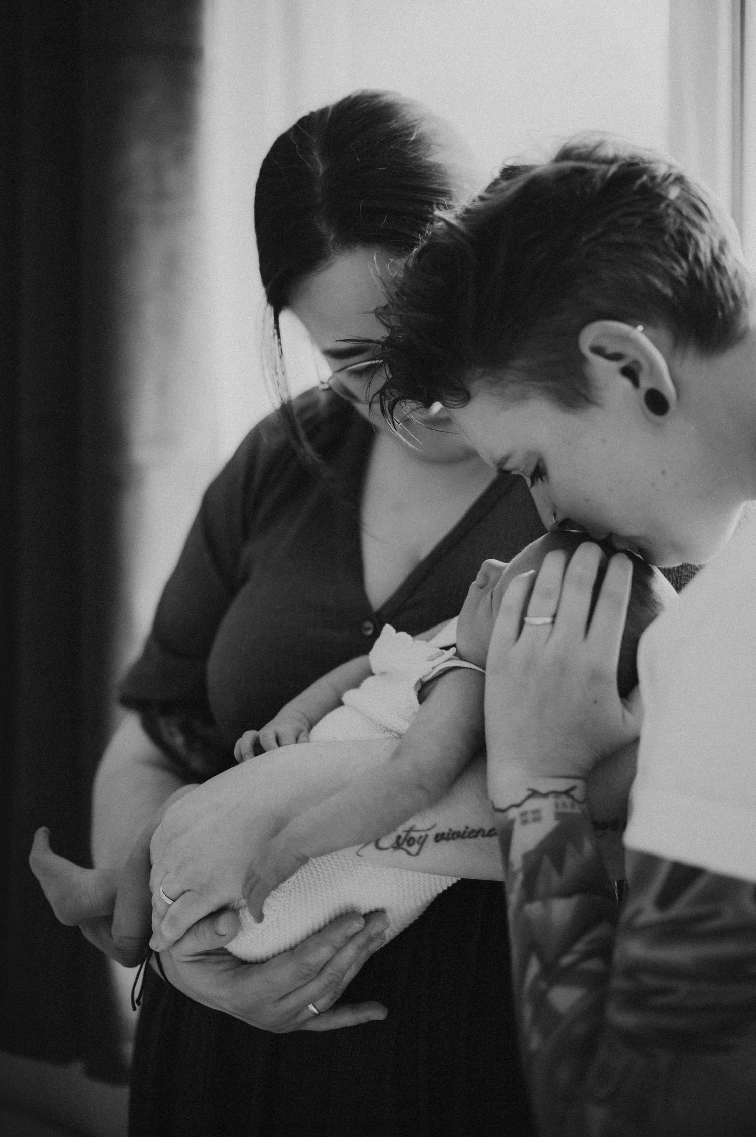 Black and white photo of two parents smiling down at their newborn baby.