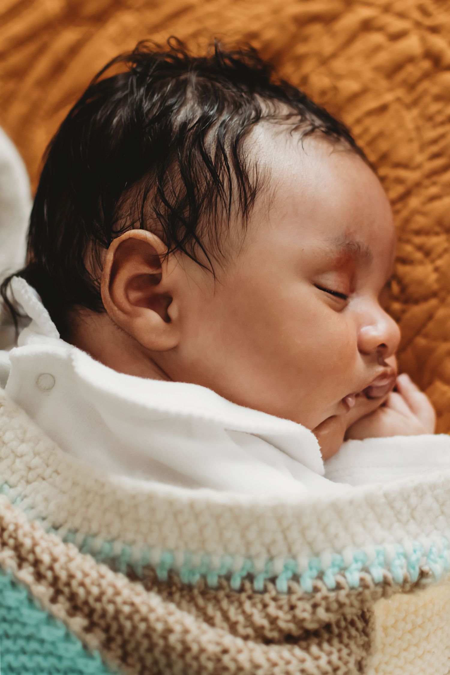 Close-up of a peaceful sleeping newborn baby with dark hair wrapped in a knit blanket.