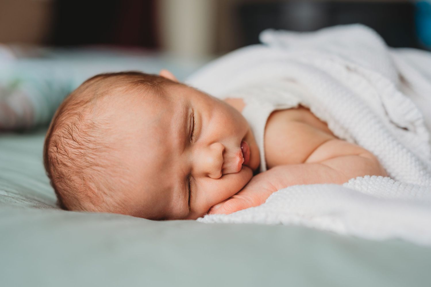 Peaceful newborn baby sleeping on a soft white blanket with a gentle smile.