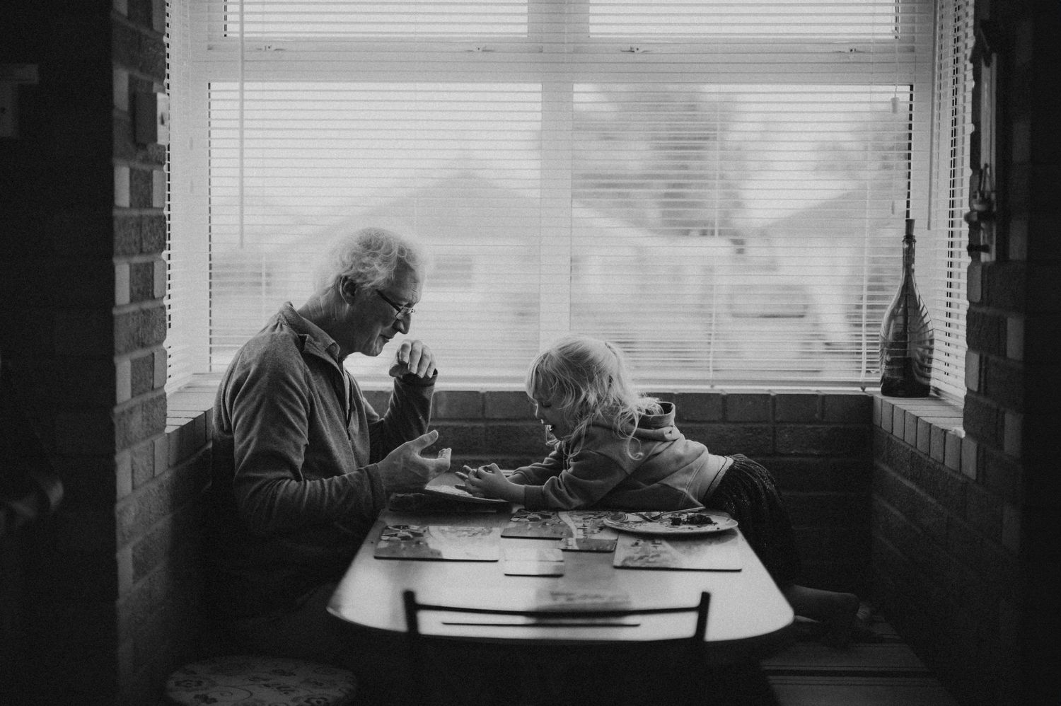 A black and white intimate photo of two elderly people sharing a quiet meal together by a window.