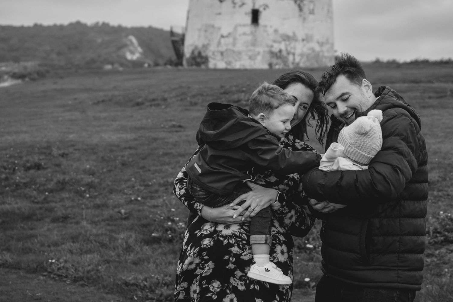 Black and white photo of a family embracing with young children near a historic stone tower.