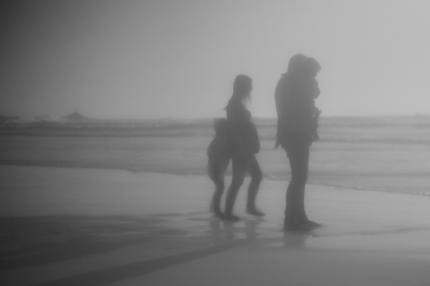 Black and white silhouette of two people standing on a misty beach shoreline.