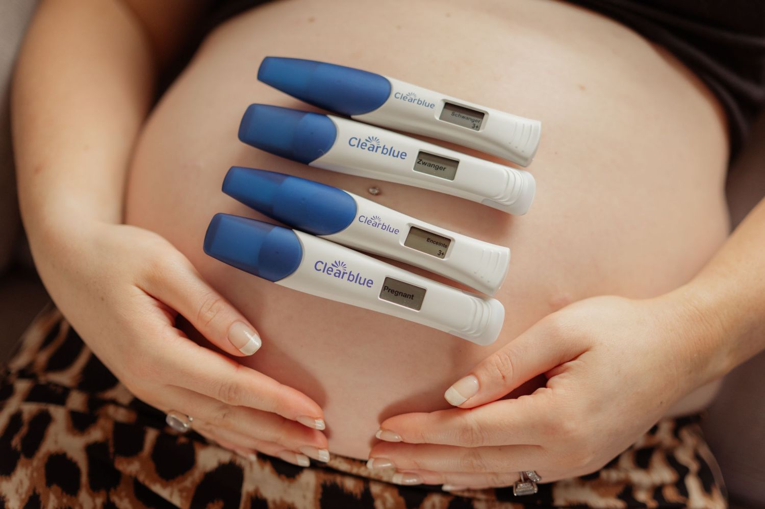Pregnancy tests resting on pregnant belly held by hands.