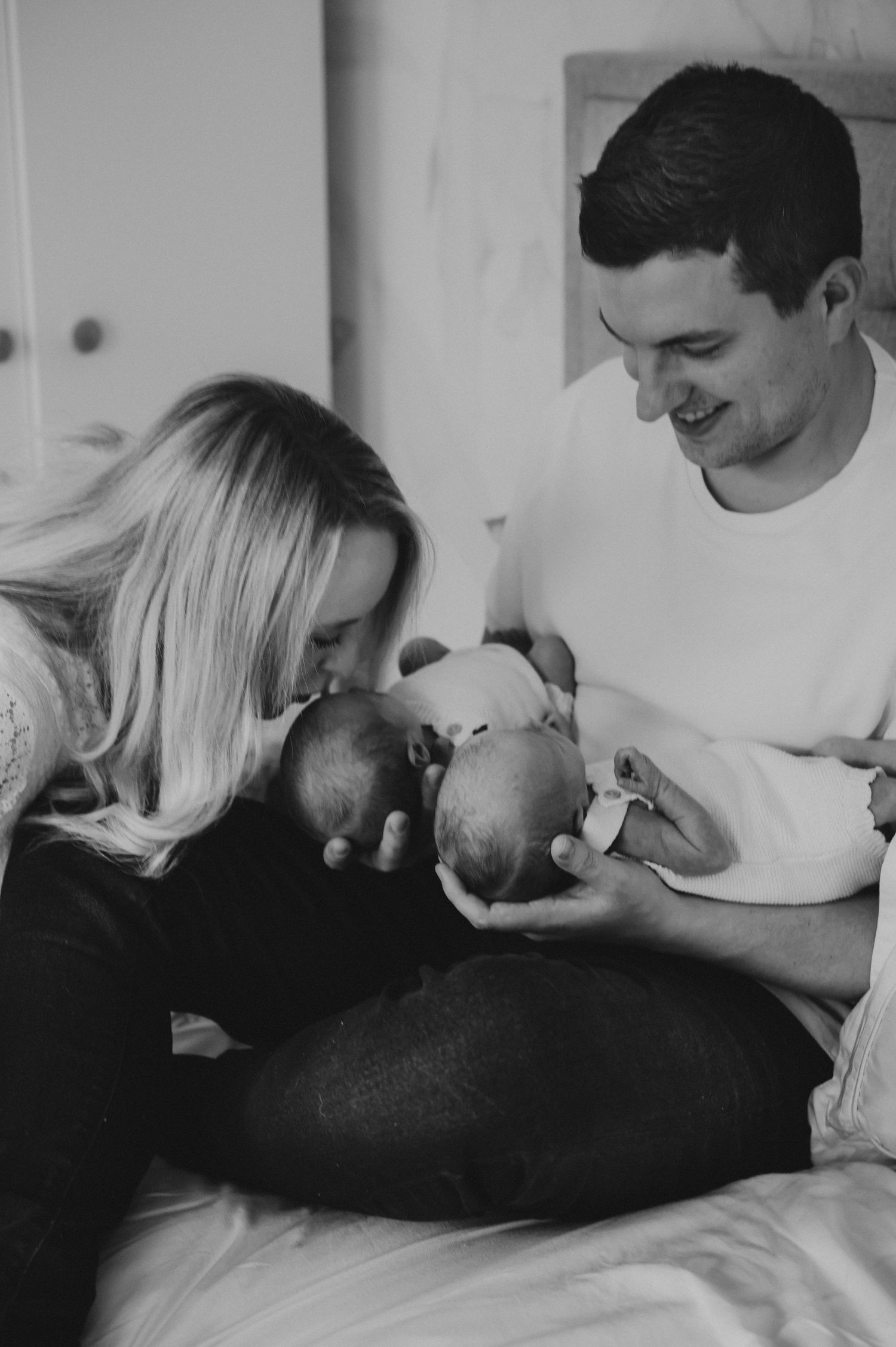 A smiling couple in black and white photo tenderly holding their newborn twins together.