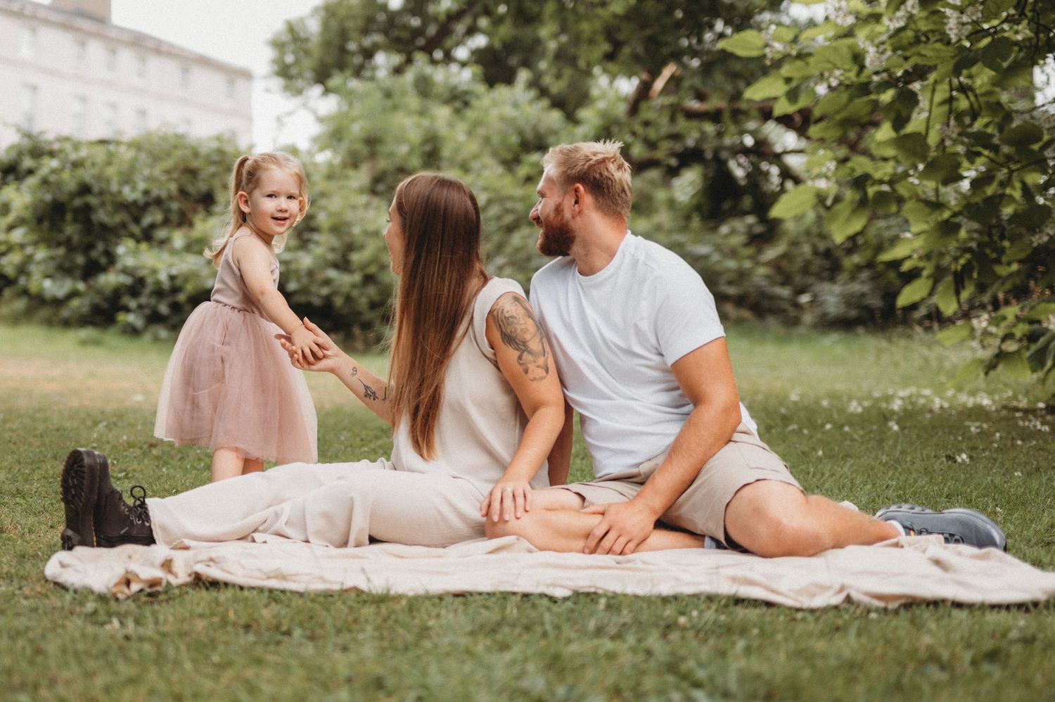 Happy young family relaxing on blanket in green park with toddler daughter.