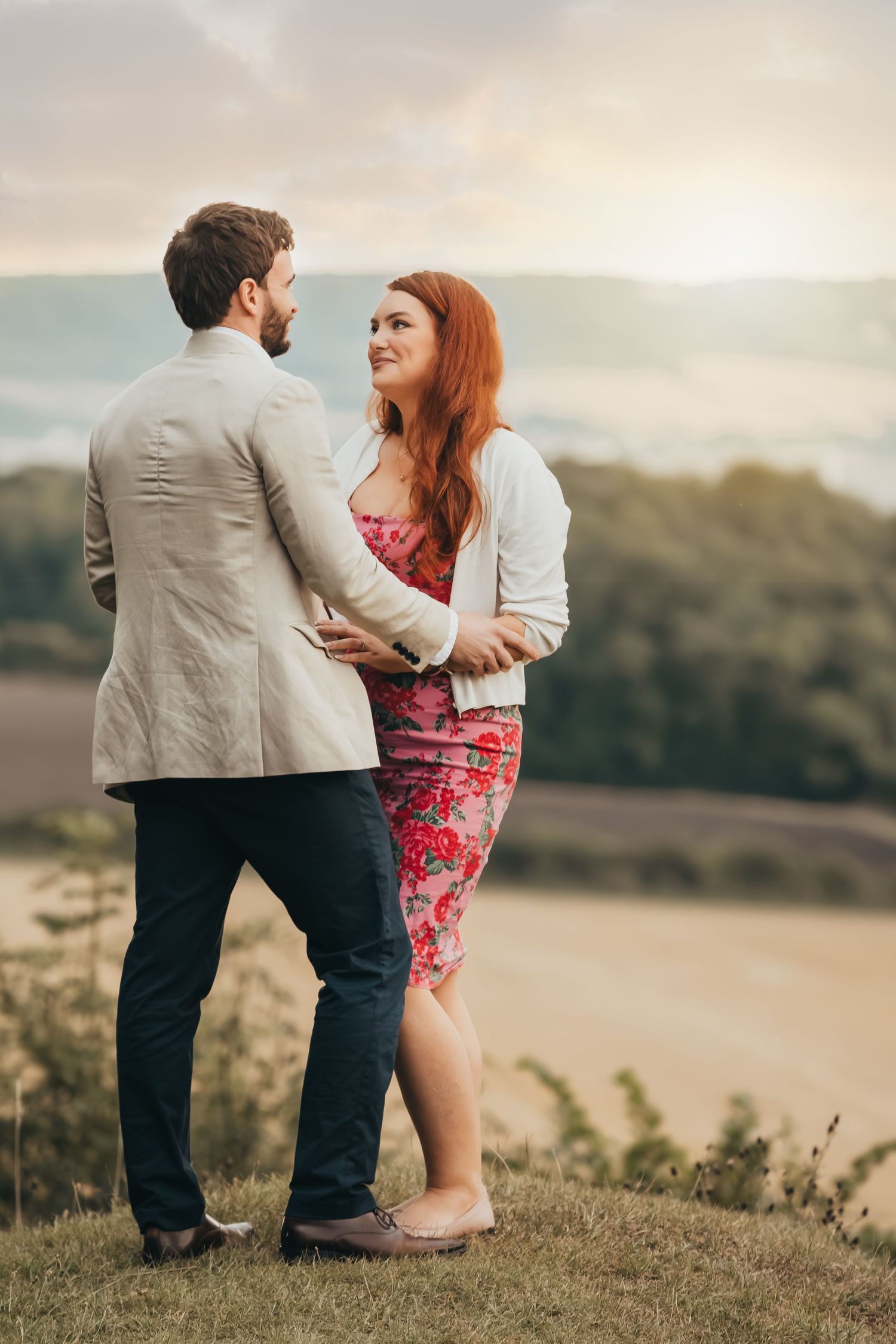 Romantic couple embracing at sunset overlooking a scenic countryside valley.